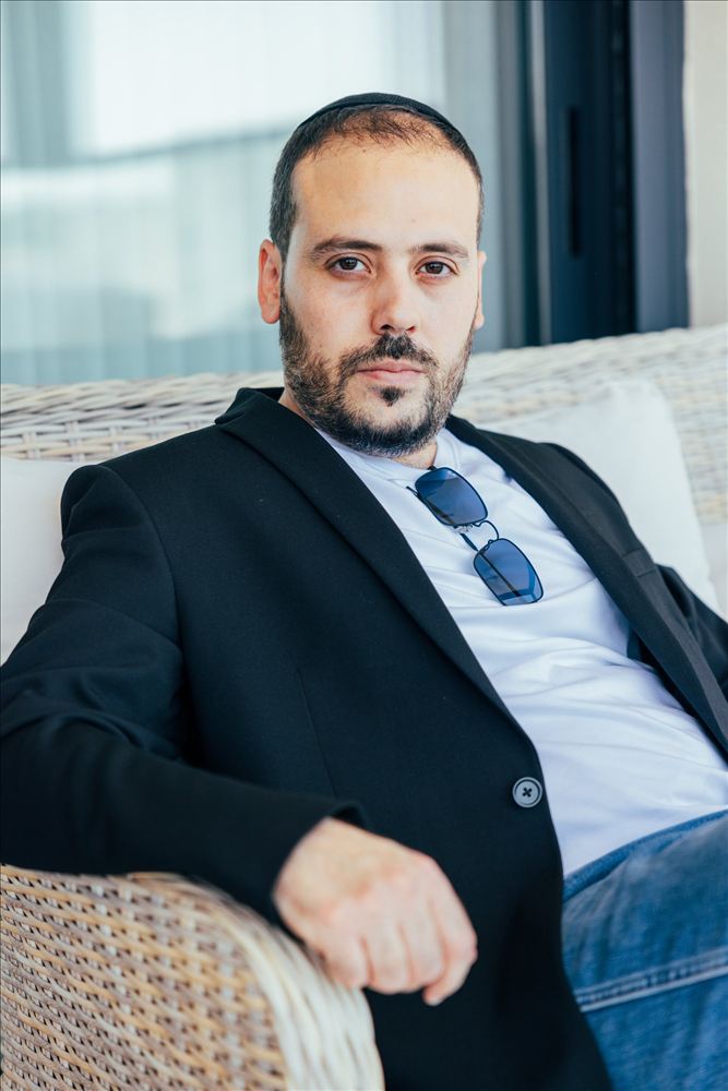 גבר בבלייזר כהה יושב על כורסת נצרים